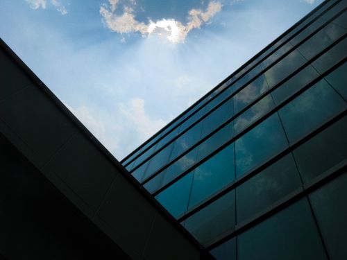 Free Low-angle view of a modern glass building reflecting the sky and sunrays Stock Photo