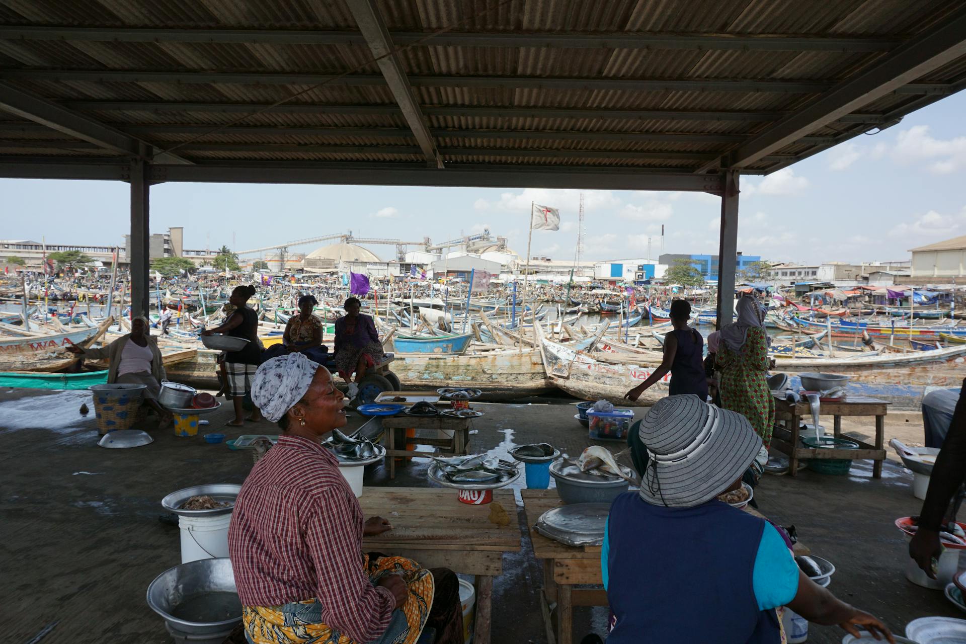 Women at Tema fish market in Ghana, bustling with boats and local vendors.