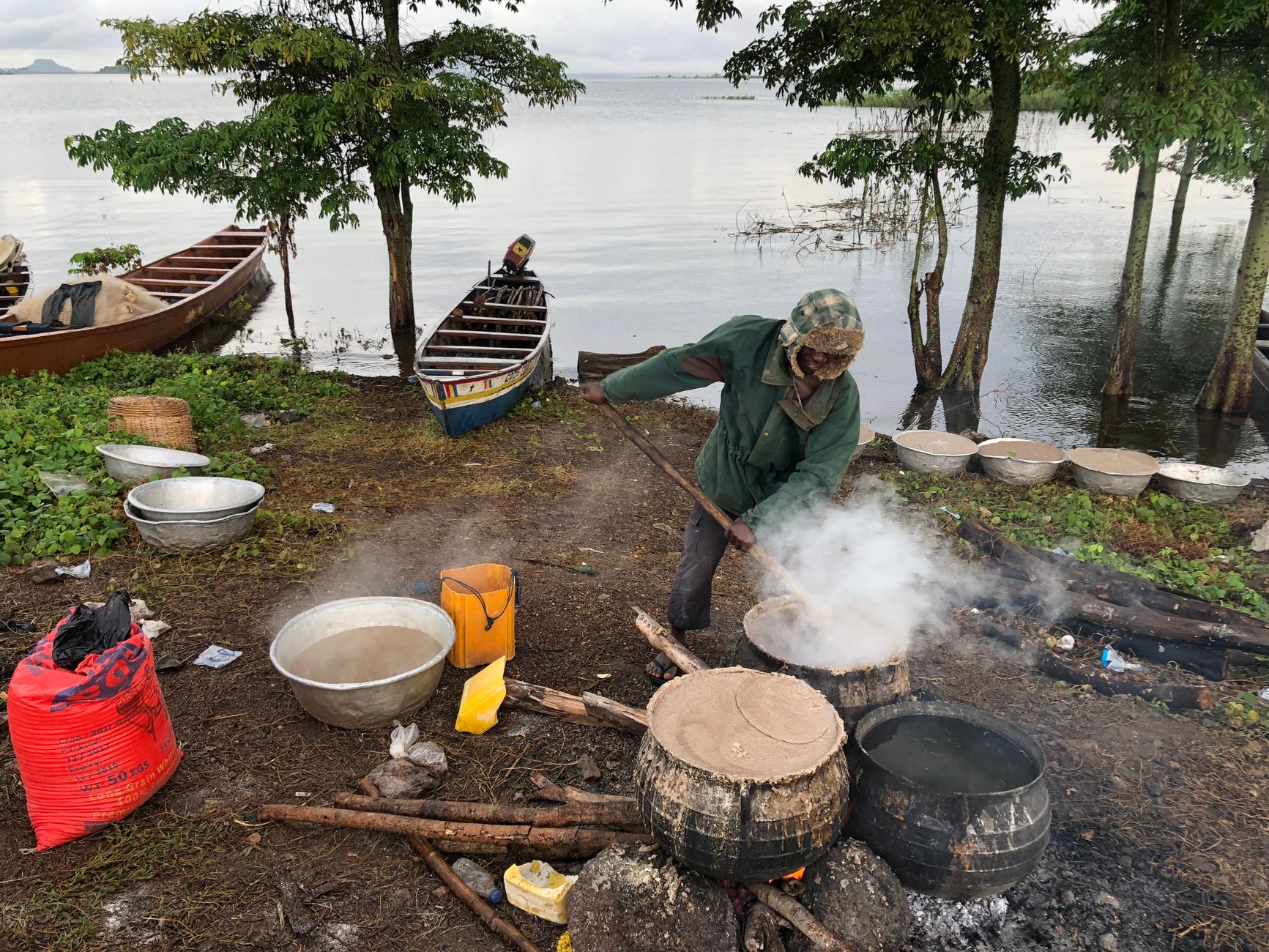 A man cooking over an open fire by a lake in Kpando, Ghana. Traditional outdoor cooking setup.