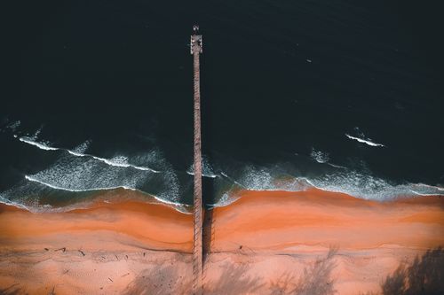 Free Dramatic aerial photo capturing a boardwalk stretching into the ocean along a vibrant beach. Stock Photo