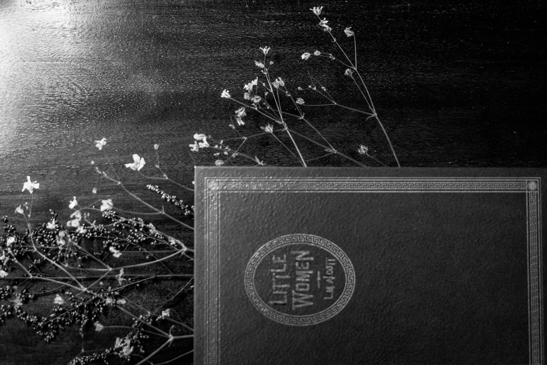 Black and white photo of 'Little Women' book with dried floral arrangement.