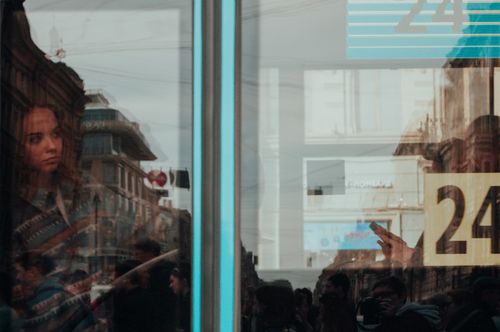 Free A woman looks through a glass window in a bustling urban environment, capturing reflections and city life. Stock Photo