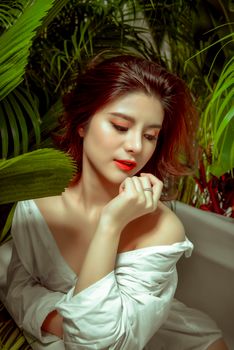 Beautiful woman with red lips surrounded by lush green plants, evoking elegance and serenity.