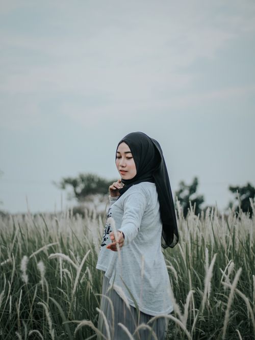Free A Muslim woman in hijab stands gracefully in an Indonesian field, capturing natural beauty. Stock Photo
