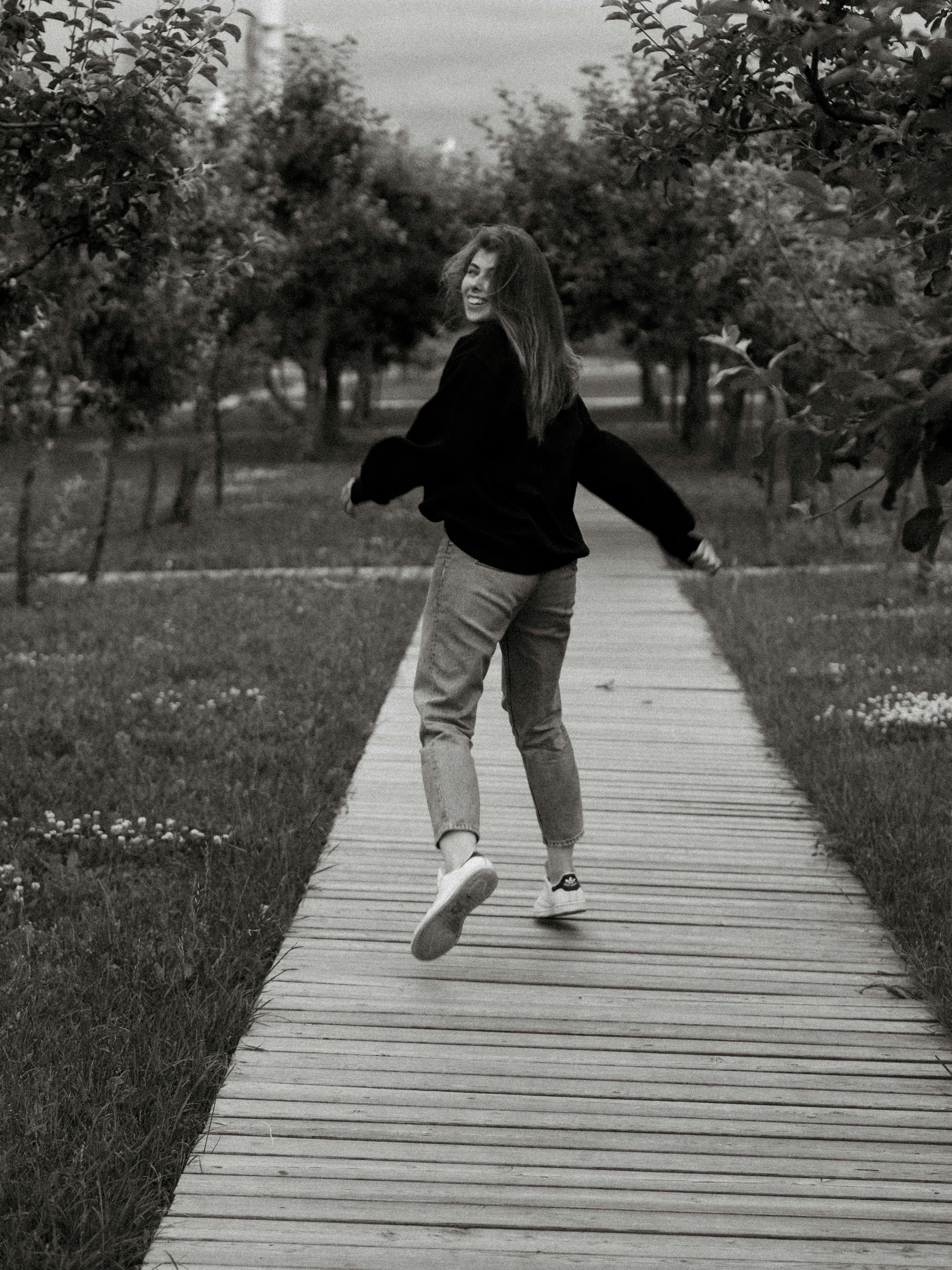Black and white image of a woman joyfully running on a boardwalk in nature.