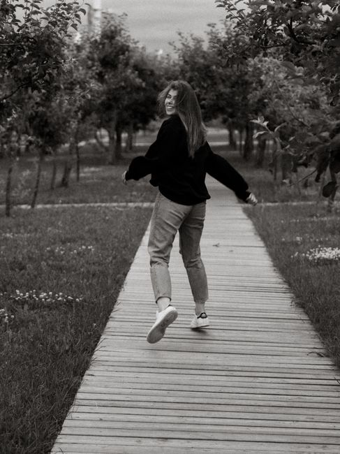 Black and white image of a woman joyfully running on a boardwalk in nature.