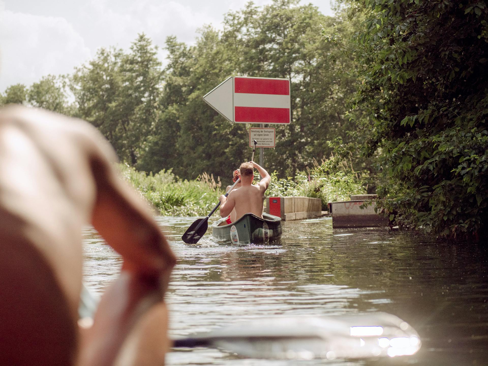 Two men kayaking through a lush, serene waterway in Germany on a sunny day.