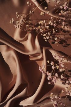 Textured satin fabric with delicate dried flowers in a soft, natural composition.