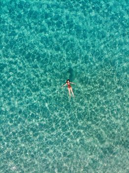 Aerial shot of a woman swimming in clear turquoise waters of Geremeas, Sardegna.