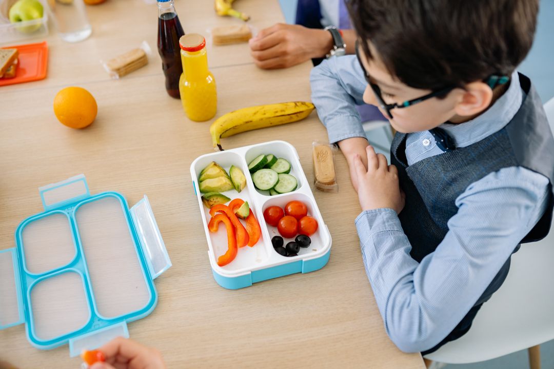 Child Nutrition Guide: What to Feed Kids (Chef-Approved) 2 A school-age boy sitting at a table, happily eating a nutritious lunch from a colourful tiffin lunchbox.