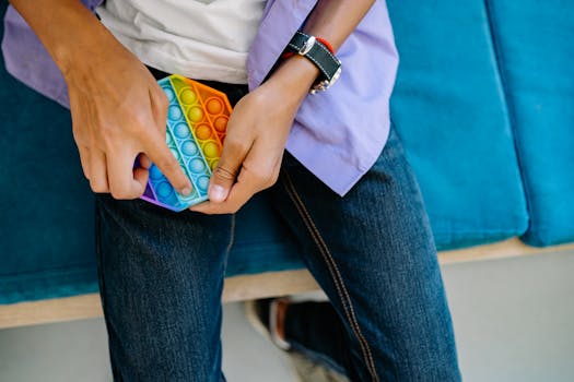 Close-up of person playing with a colorful Pop It toy on denim jeans while sitting.