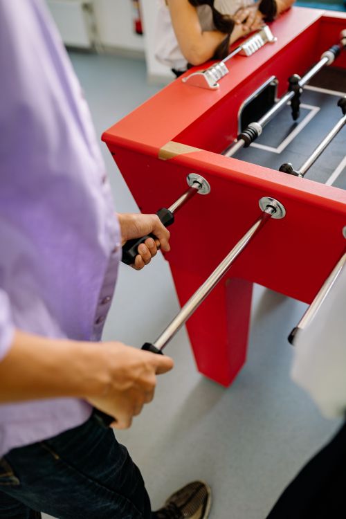 Free Close-up of adults playing a vibrant red table football game indoors. Stock Photo