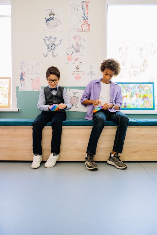 Free Two boys sitting and playing with colorful fidget toys in a creative classroom setting. Stock Photo