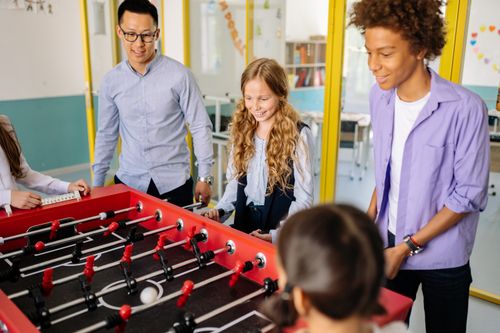Free Group of children and a teacher playing foosball indoors, promoting fun learning. Stock Photo