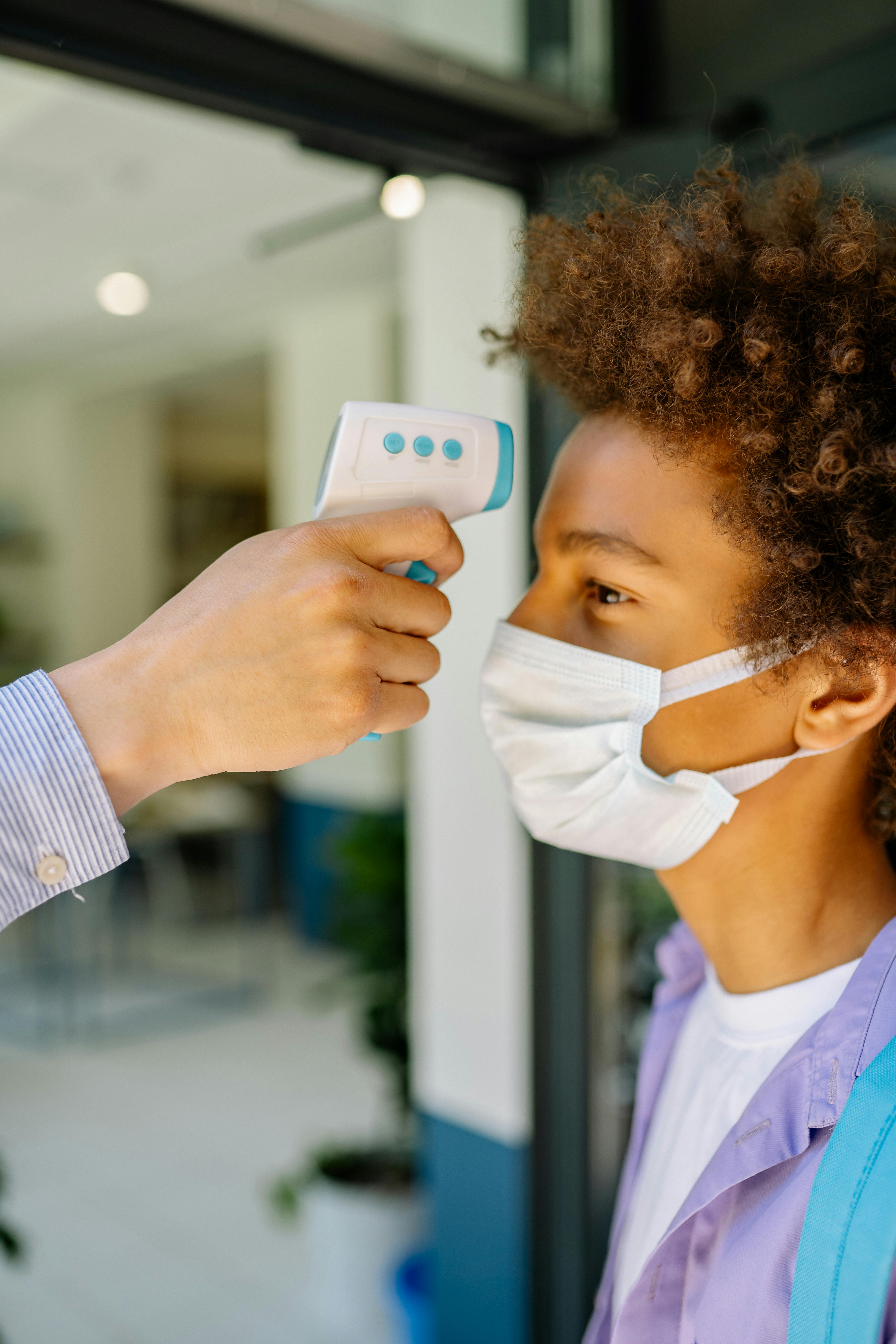 A young boy wearing a mask getting his temperature checked at school during COVID-19 pandemic.