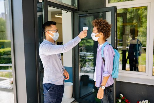 Teacher checks student's temperature with an infrared thermometer outside school.