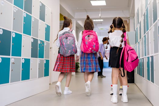 Three school girls with backpacks walking in a school corridor lined with lockers.