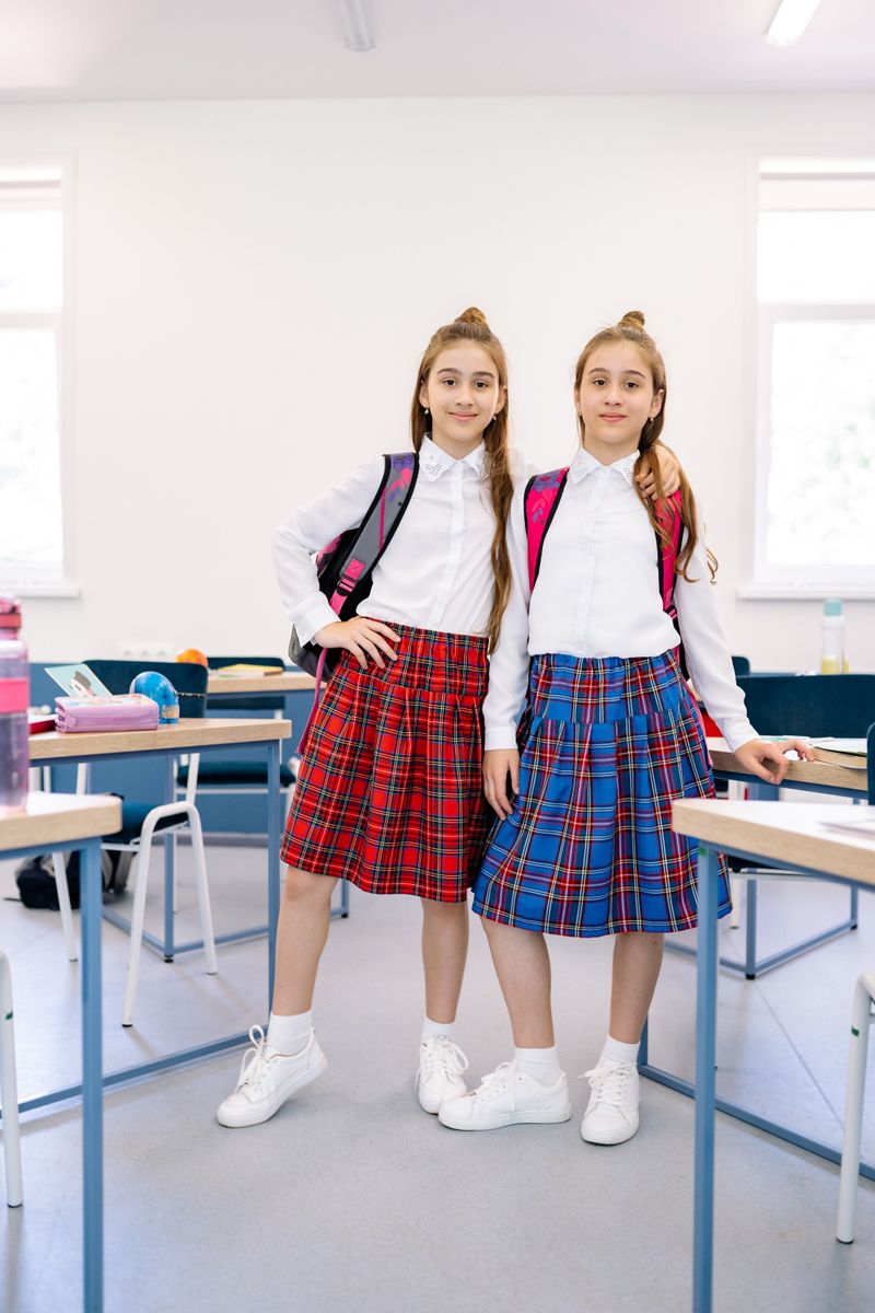 Two students in plaid uniforms in a bright classroom