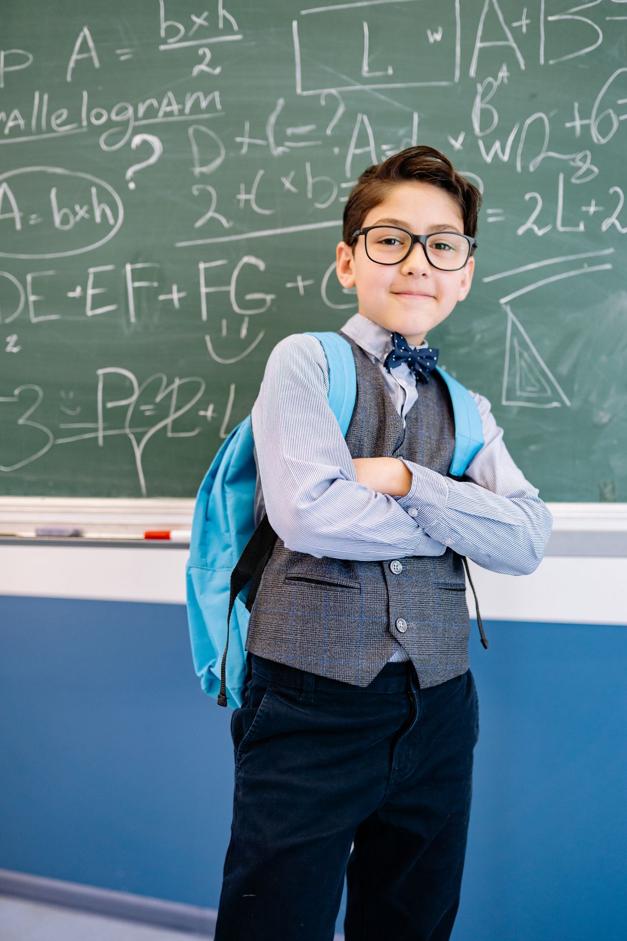 Enfant confiant avec un sac à dos devant un tableau noir, prêt pour sa transition vers l'école primaire.