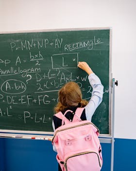 Young student writing math formulas on a blackboard in a classroom, focused on learning.