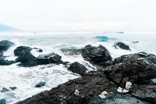 Dynamic seascape with powerful waves crashing against dark coastal rocks under a cloudy sky.