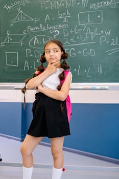 Caucasian girl poses thoughtfully by a chalkboard filled with math equations, wearing a school uniform.