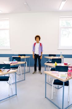 Teenager standing in a well-lit classroom with tables and chairs, conveying a back-to-school theme.