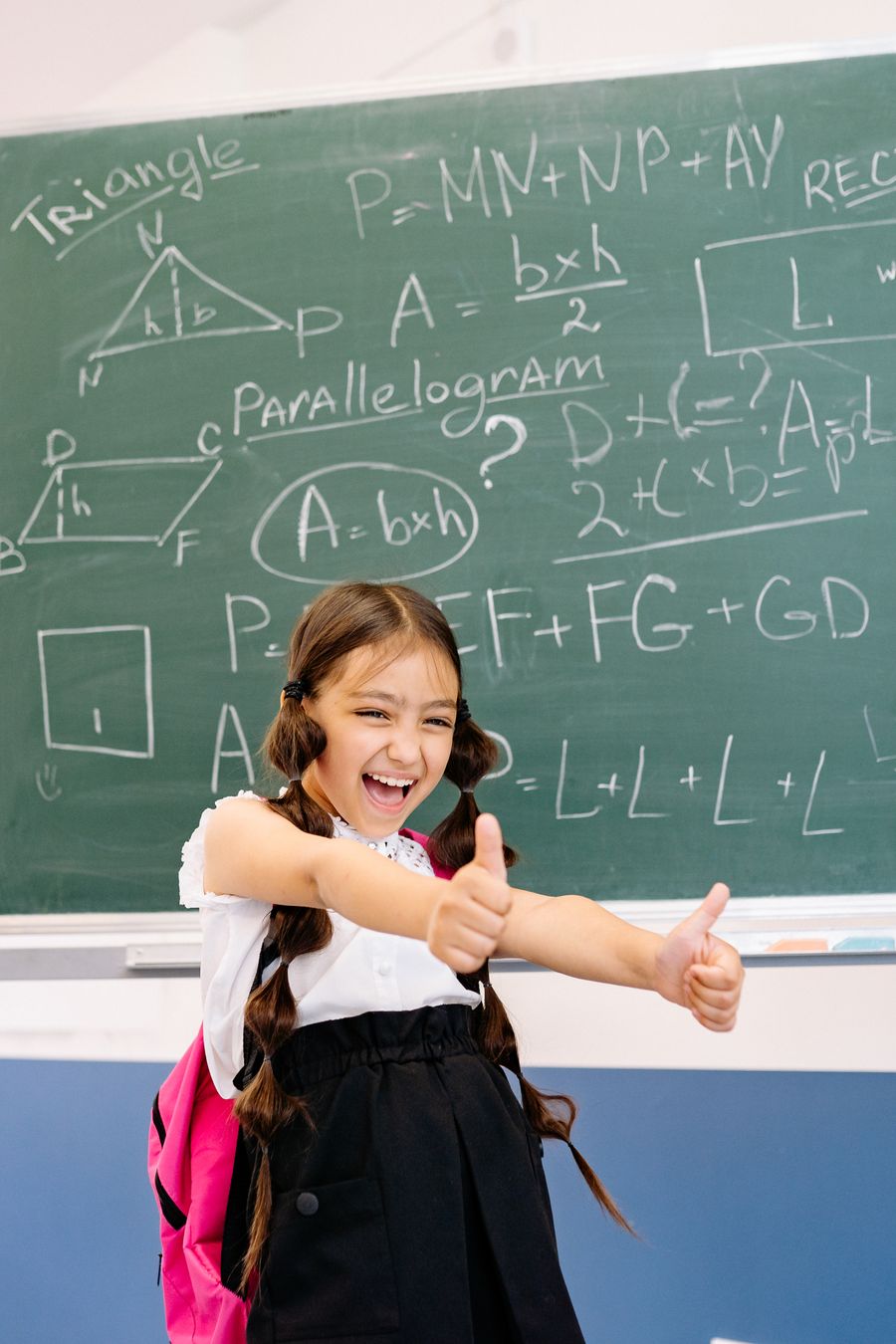 Happy elementary student giving a thumbs up in front of a math chalkboard