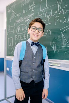 Smiling boy in formal attire stands in front of a chalkboard filled with equations.