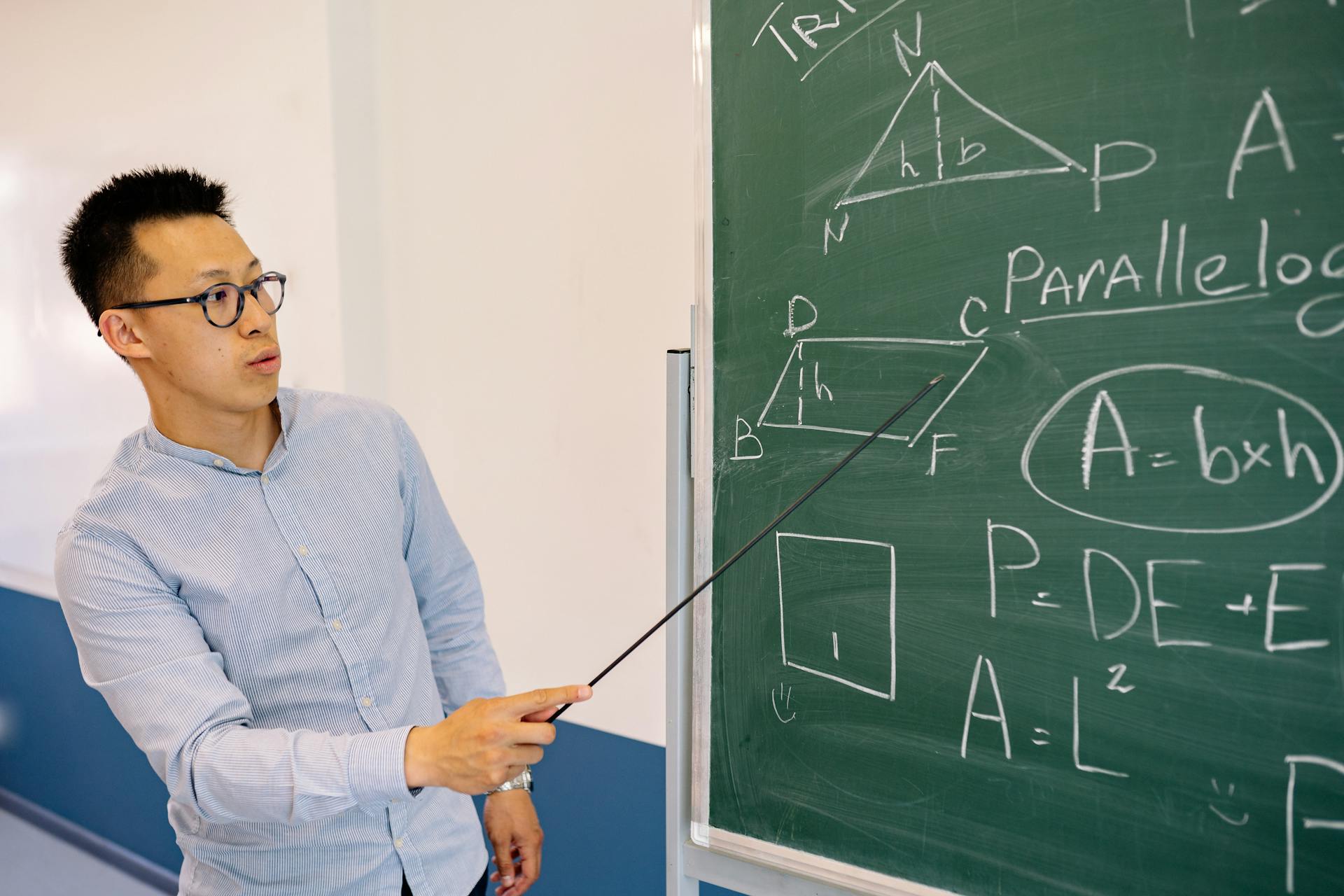 Math teacher demonstrating equations on the blackboard in classroom setting.