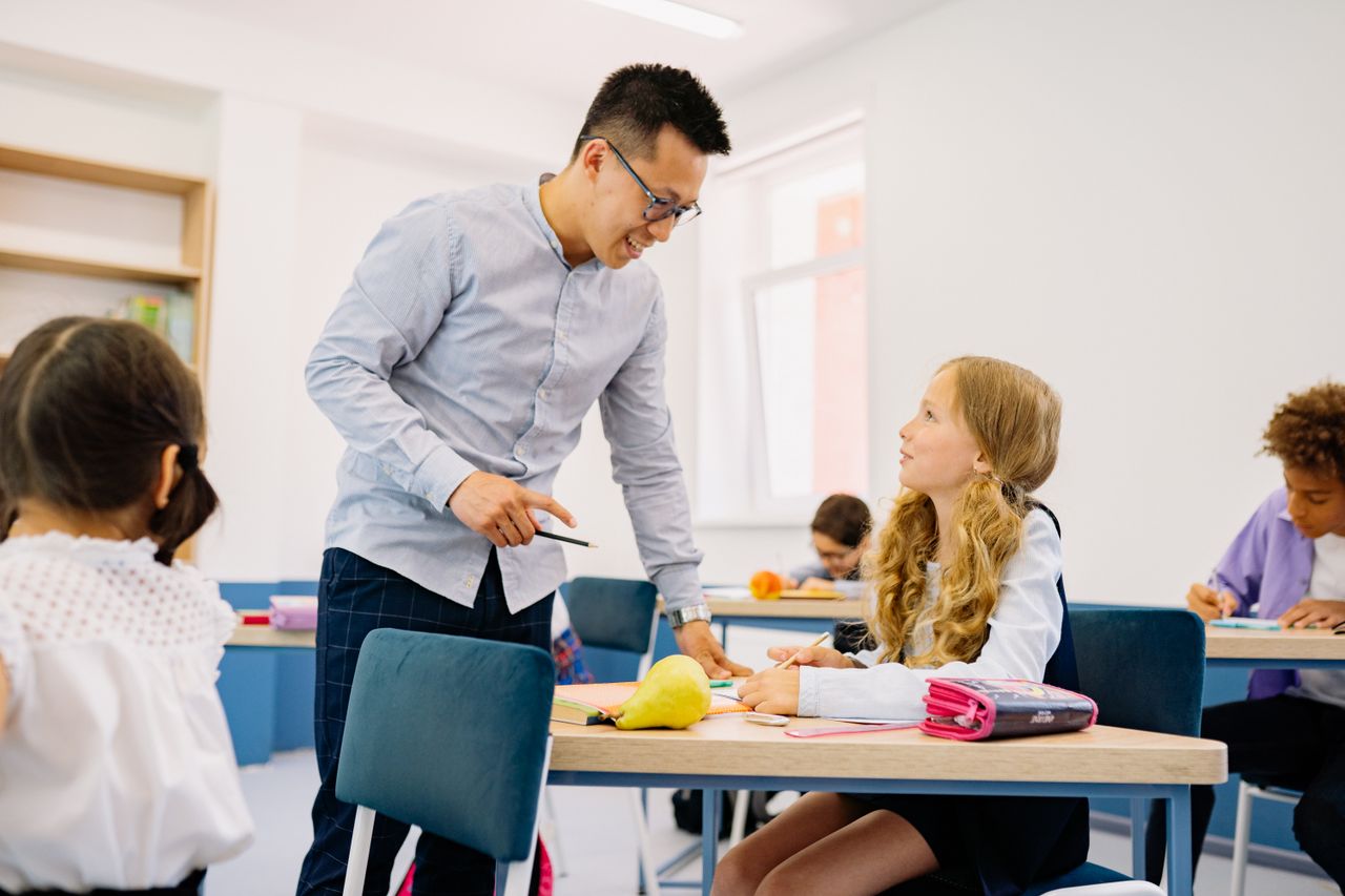 A male teacher interacting with diverse students in a bright classroom setting, promoting active learning.