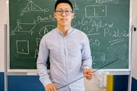 A Male Teacher Holding a Pointing Stick in Front of a Blackboard