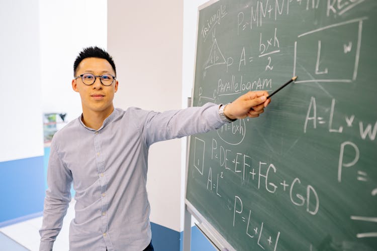 Man Wearing Eyeglasses Pointing At The Blackboard