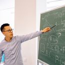 Man in Gray Crew Neck Long Sleeve Shirt Holding Pen Writing on Chalk Board