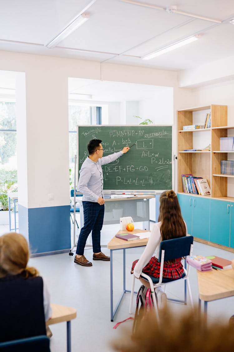 A Man Pointing At A Blackboard While Teaching A Class