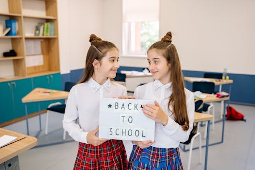 Smiling twins in school uniforms hold a 'Back to School' sign in a bright classroom.