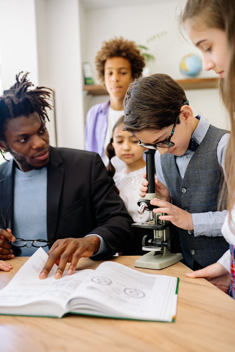 A Boy Using A Microscope Beside His Teacher