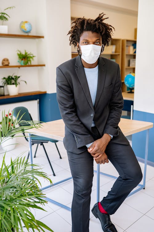 Free A Man in Black Suit and Pants Sitting on the Table while Wearing Face Mask Stock Photo