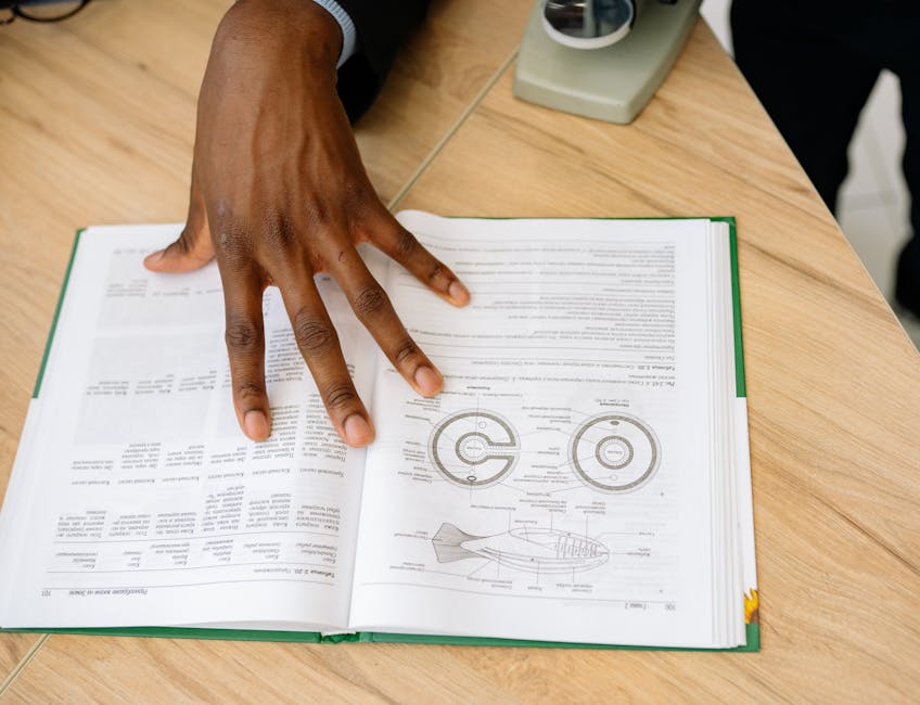 A hand placed on an open scientific book with diagrams, highlighting research or learning.