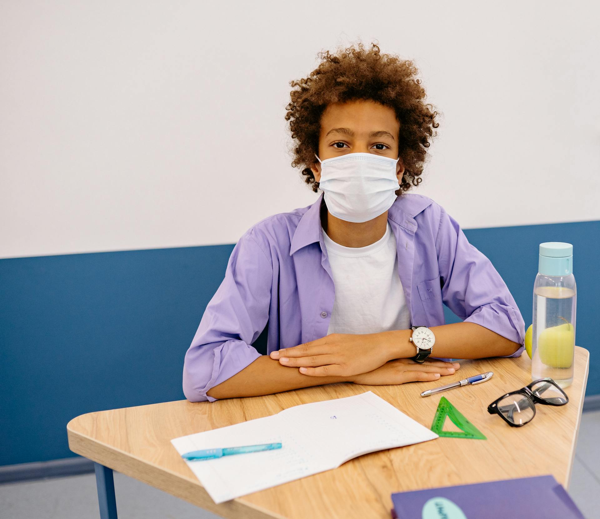 Male Student Sitting by the Wooden Table while Wearing a Face Mask