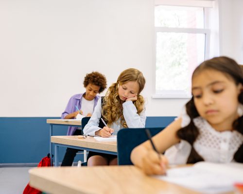 Free Children focused on writing assignments during a classroom lesson, sitting at desks. Stock Photo