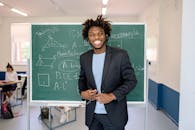 Man in Black Blazer Standing Near Chalkboard