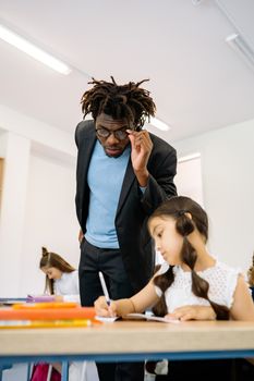 Teacher assisting young student with learning in a bright classroom environment.