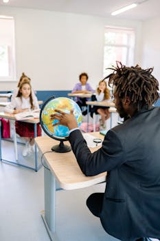 A teacher explains geography to an attentive class using a globe in a bright classroom setting.