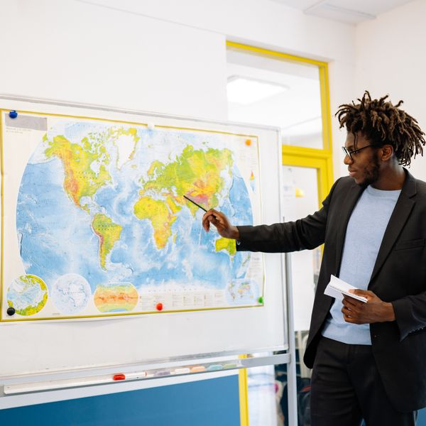 Professor apontando para o mapa-múndi durante a aula: Licenciatura em História EAD em 2 anos