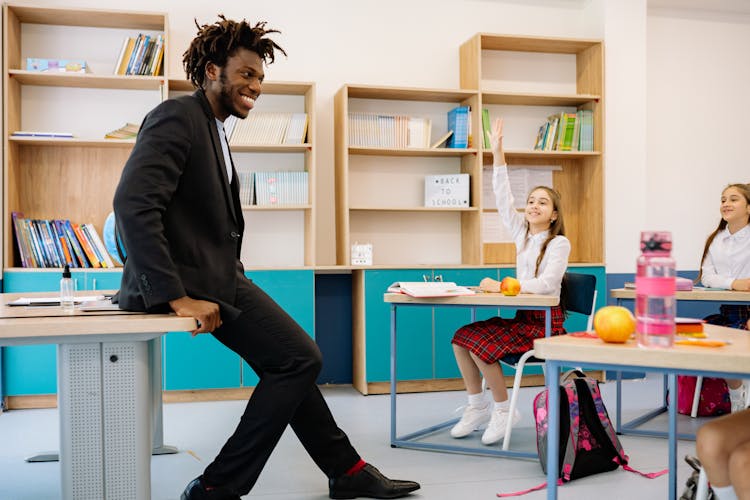 Male Teacher Sitting On The Table In Front Of The Students