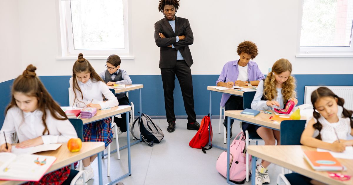 Teacher standing among students working at their desks in a bright classroom