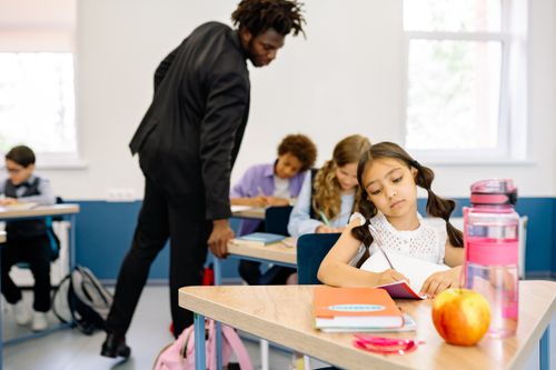 Free A classroom scene with children studying while a teacher provides guidance, fostering learning. Stock Photo