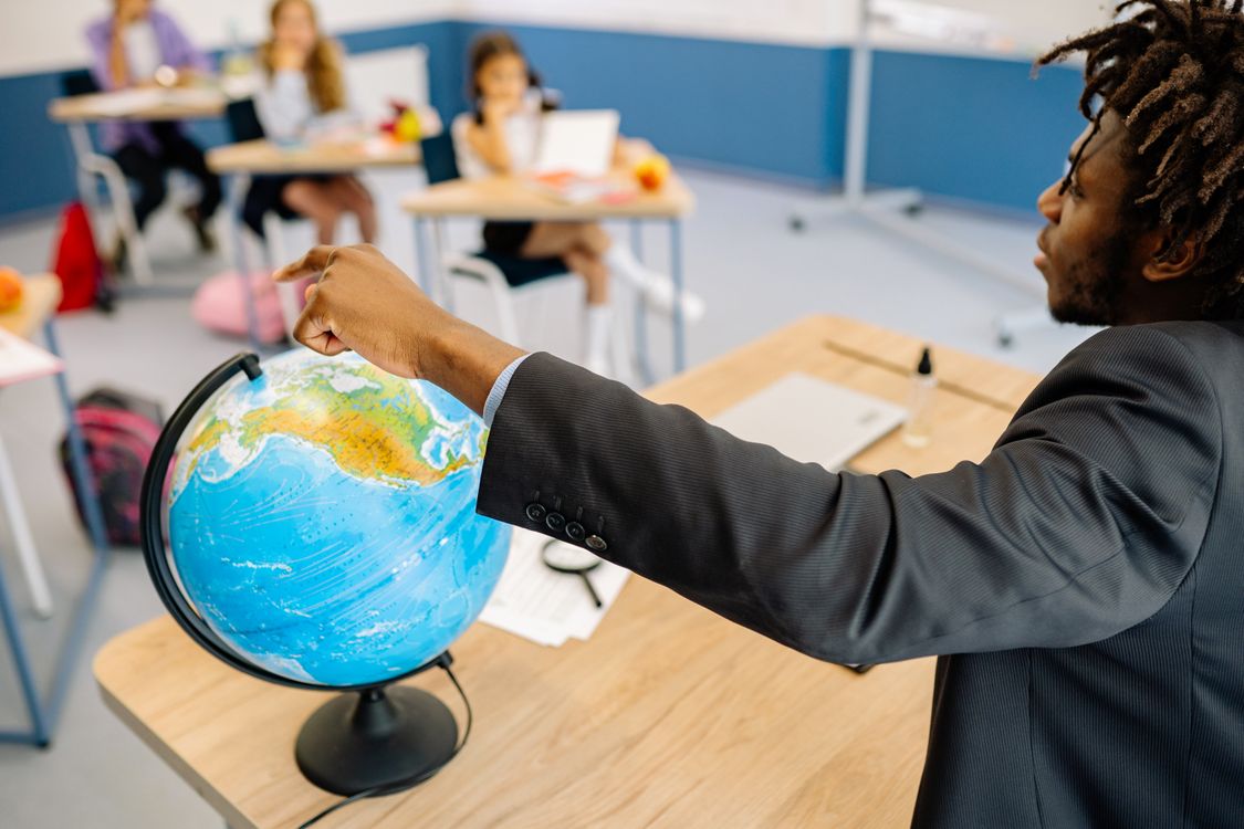 Free A teacher points to a globe in a classroom, engaging students in a geography lesson. Stock Photo