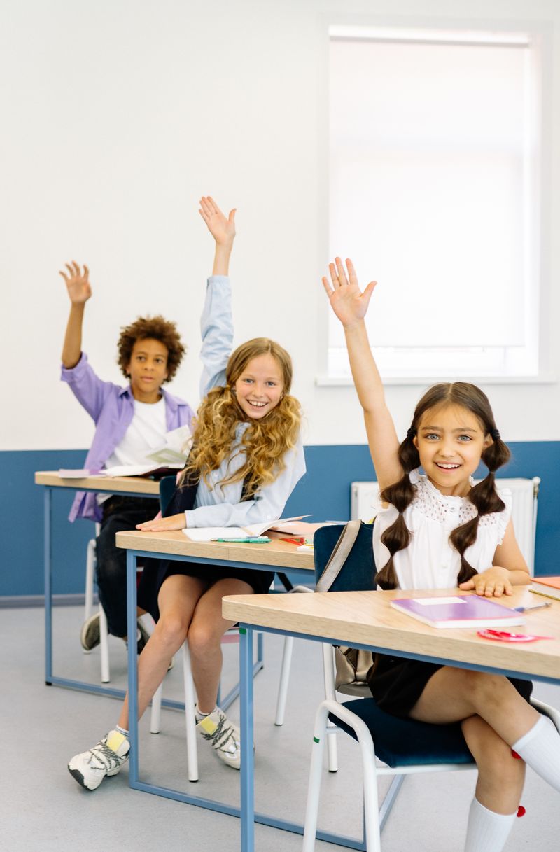 Engaged diverse students in classroom raising hands with enthusiasm
